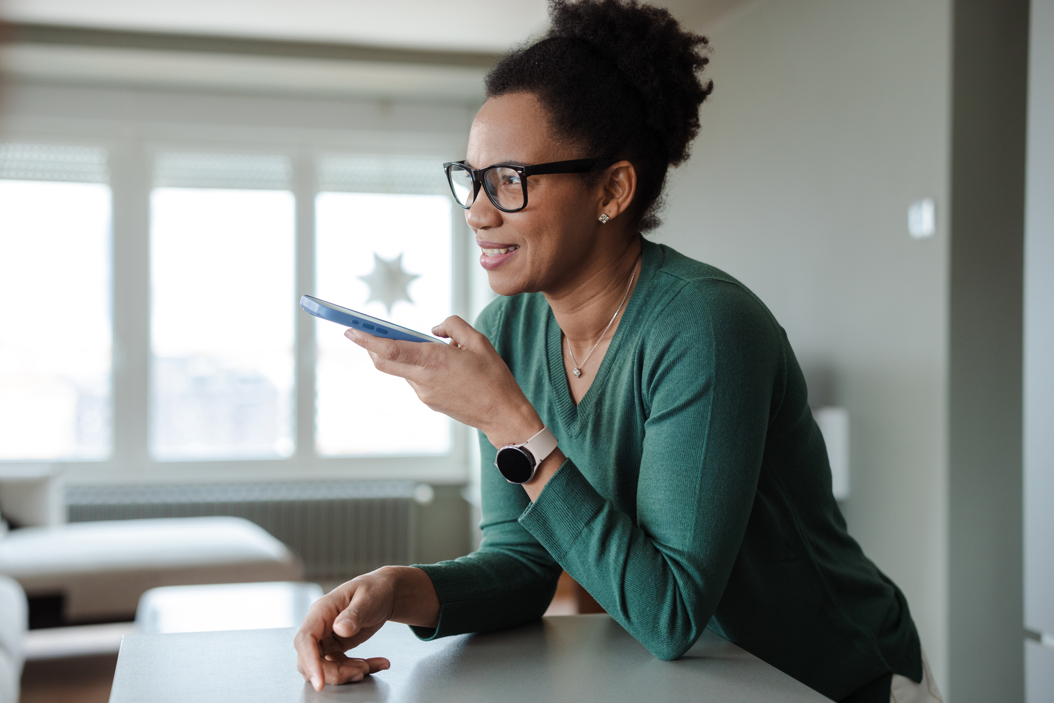 A person leans on a kitchen bench while having a relaxed conversation on a smart phone.
